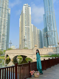 Woman standing by modern buildings against sky