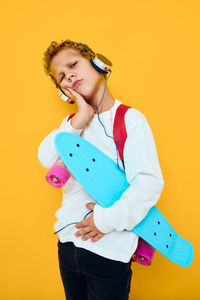 Portrait of young woman standing against yellow background