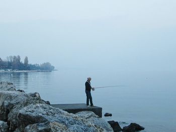 Side view of man fishing in lake against sky