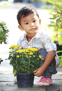 Portrait of cute boy holding potted plant while crouching on footpath