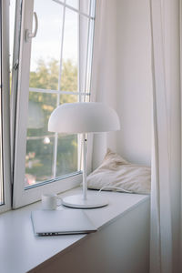 Close-up of electric lamp on table by window at home