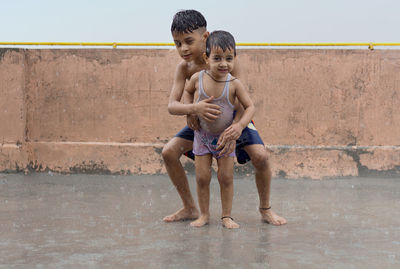 Two kids playing and having fun in rain at their terrace, outdoors during monsoon season.