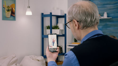 Rear view of man talking with doctor on phone at home