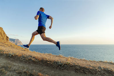 Male runner run uphill in background sky and sea