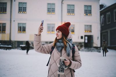 Young woman using phone while standing in city during winter