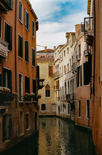 Residential buildings by canal against sky in city