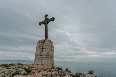 Metal cross on a brick monolith on top of a mountain, on a foggy and cloudy day.