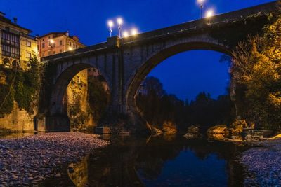 Arch bridge over river against sky at night