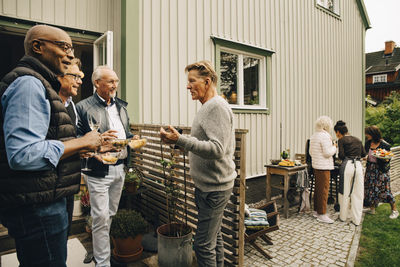 Senior men talking and enjoying snacks while women are preparing dinner at back yard