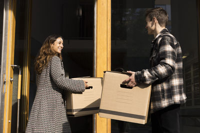 Multiracial couple assisting each other while carrying boxes during relocation of house