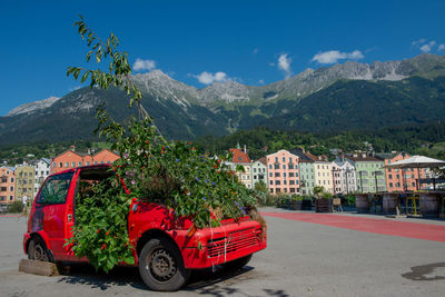 Red car on street by buildings in city against sky