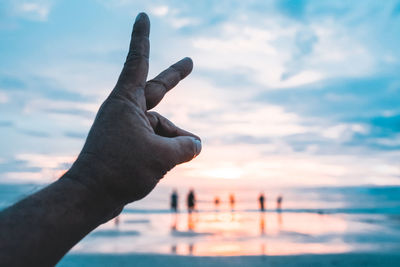 Cropped image of person hand against sea during sunset