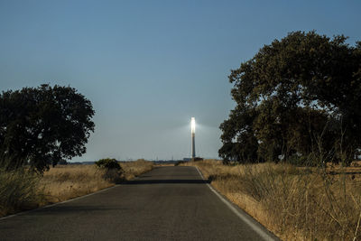 Road amidst trees on field against clear sky