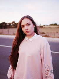 Portrait of beautiful young woman standing on road against sky