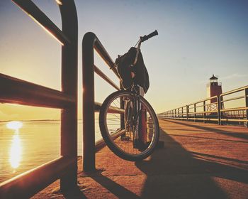 Bicycle parked on pier by lake during sunset