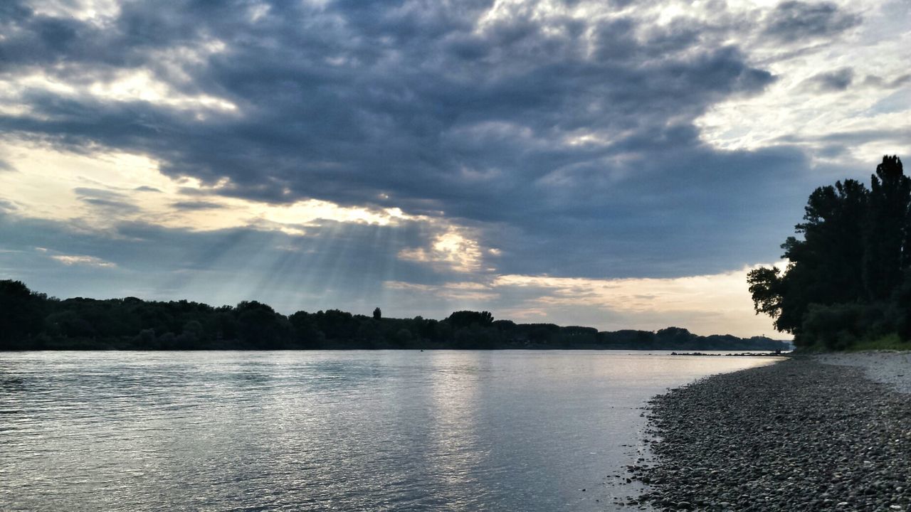 water, sky, cloud - sky, scenics, tranquil scene, beauty in nature, tranquility, cloudy, waterfront, tree, reflection, cloud, lake, nature, river, idyllic, silhouette, sunset, sunbeam, sunlight