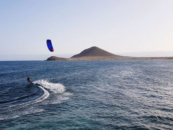 Man kiteboarding in sea against clear sky