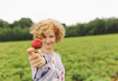 Portrait of smiling young woman showing strawberry on grassy field