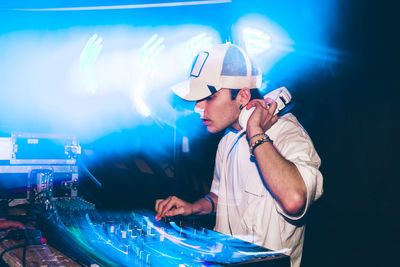 Dj with headphones at night club party under the blue light and people crowd in background