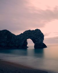 Rock formation in sea against sky during sunset