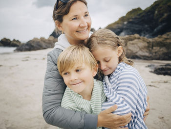 Smiling woman embracing kids standing at beach