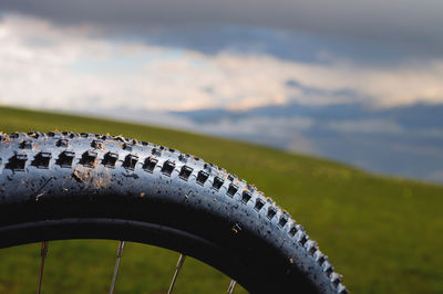 Mountain bike tire with spikes close-up, with blurred background of green mountain fields and cloudy