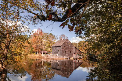 Reflection of mill and trees in lake against sky during autumn