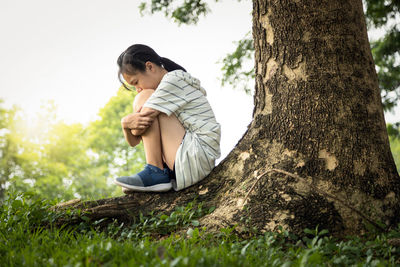 Side view of boy sitting on tree trunk