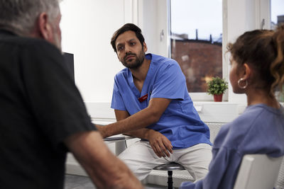 Male doctor talking to girl patient and grandfather during appointment