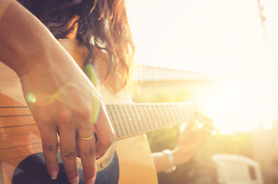 Midsection of woman playing guitar on sunny day