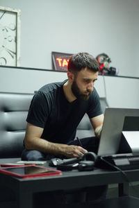 Thoughtful adult guy in casual outfit with tattoos sketching on computer in bright tattoo studio