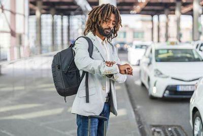 Businessman with backpack checking time in wristwatch on footpath