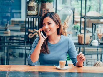 Young woman using phone while standing at cafe