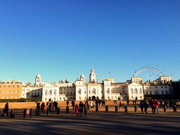 People walking by historic building against clear blue sky at st james park