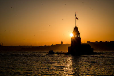 Silhouette buildings by sea against sky during sunset