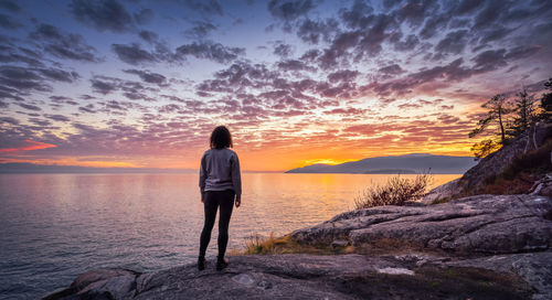 Rear view of man standing on rock against sea during sunset