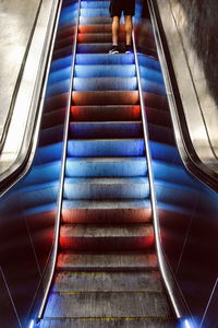 Low section of man standing on illuminated escalator