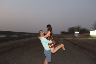 Side view of young man carrying girlfriend on beach at dusk