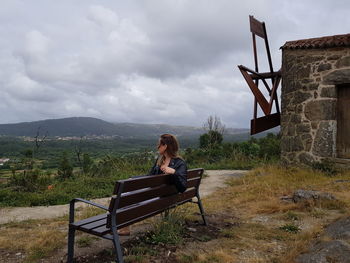 Woman sitting on bench against mountain