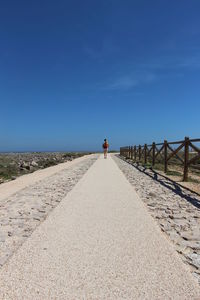 Rear view of woman on beach against clear blue sky