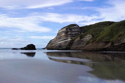 Rock formations by sea against sky at wharariki beach, south island, new zealand.