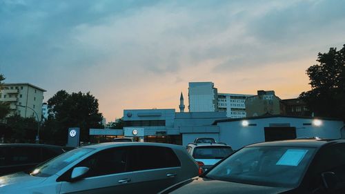 Cars on road by buildings against sky at sunset