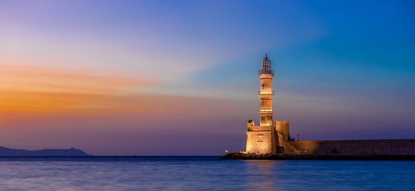 Lighthouse by sea against sky during sunset