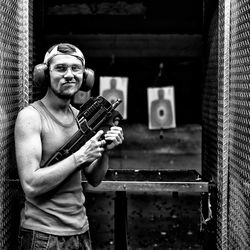 Portrait of young man holding gun while standing at target shooting range
