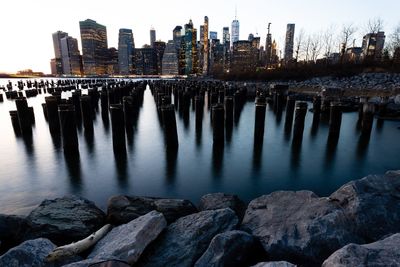 Wooden posts in river by buildings against sky