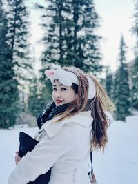 Portrait of beautiful woman standing against trees during winter