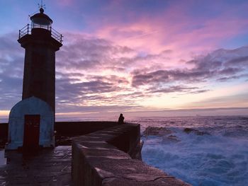 Lighthouse by sea against sky during sunset