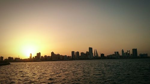 Silhouette of city at waterfront during sunset