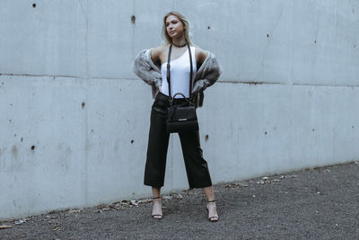 Young woman looking away while standing against wall