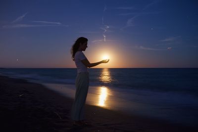 A woman on the beach holds the full moon in her hands